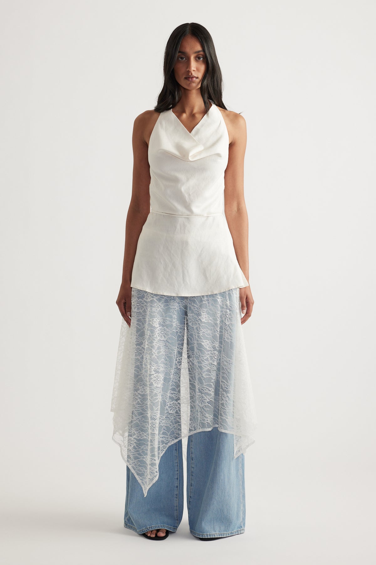 Woman wearing a white lace midi skirt over wide leg jeans with a draped asymmetric hem