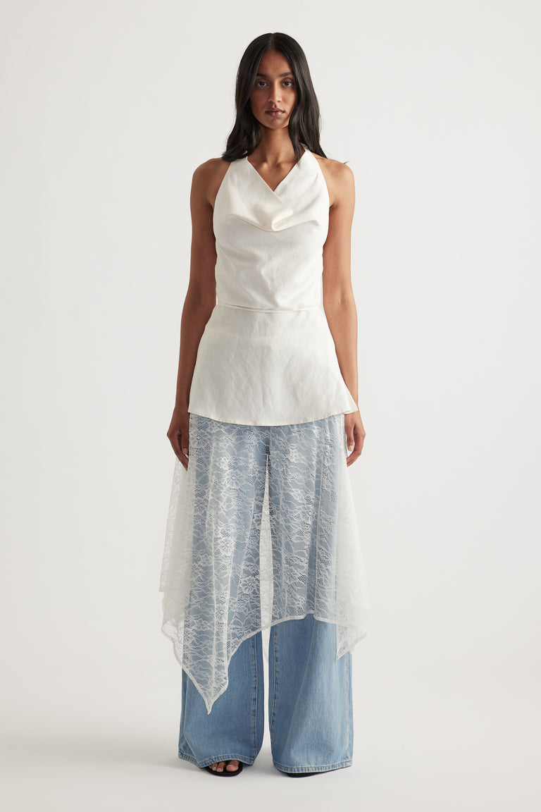 Woman wearing a white lace midi skirt over wide leg jeans with a draped asymmetric hem