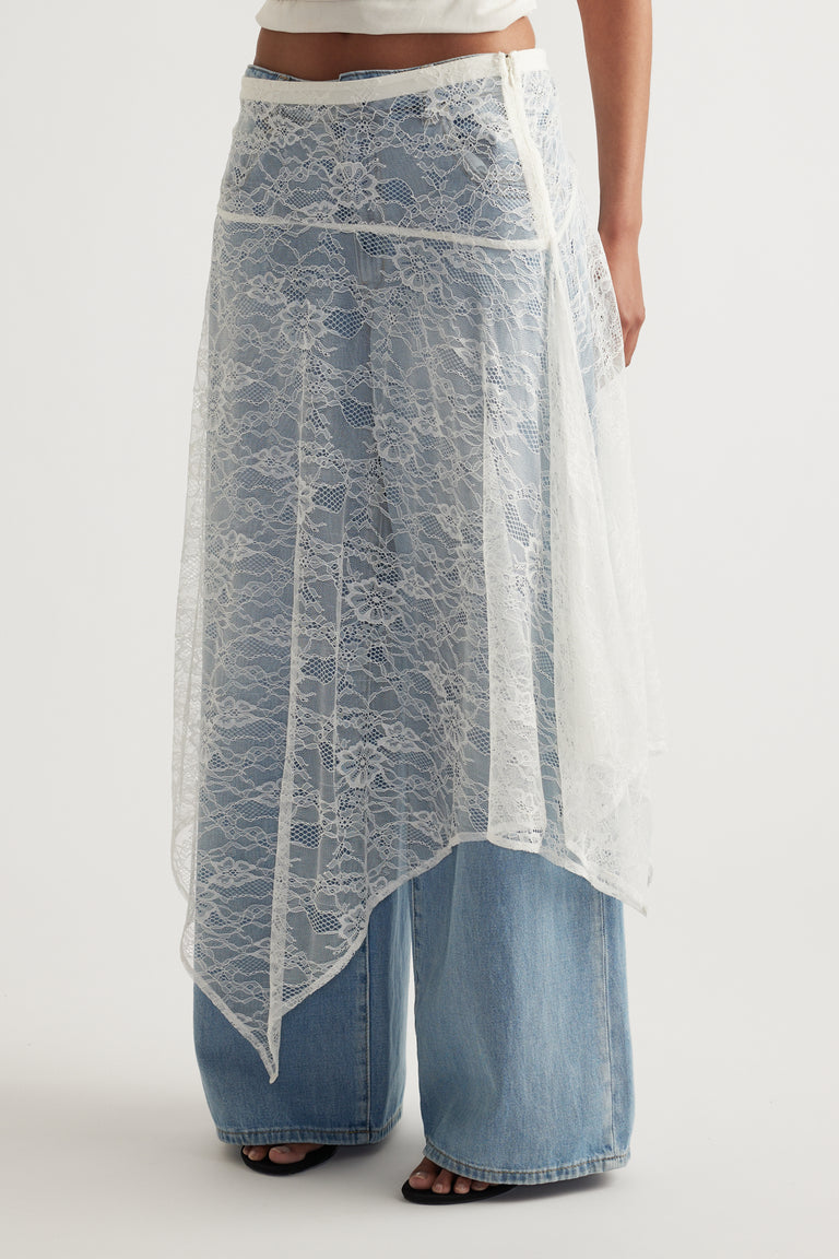 Model wearing a white lace asymmetric midi skirt layered over wide leg blue jeans