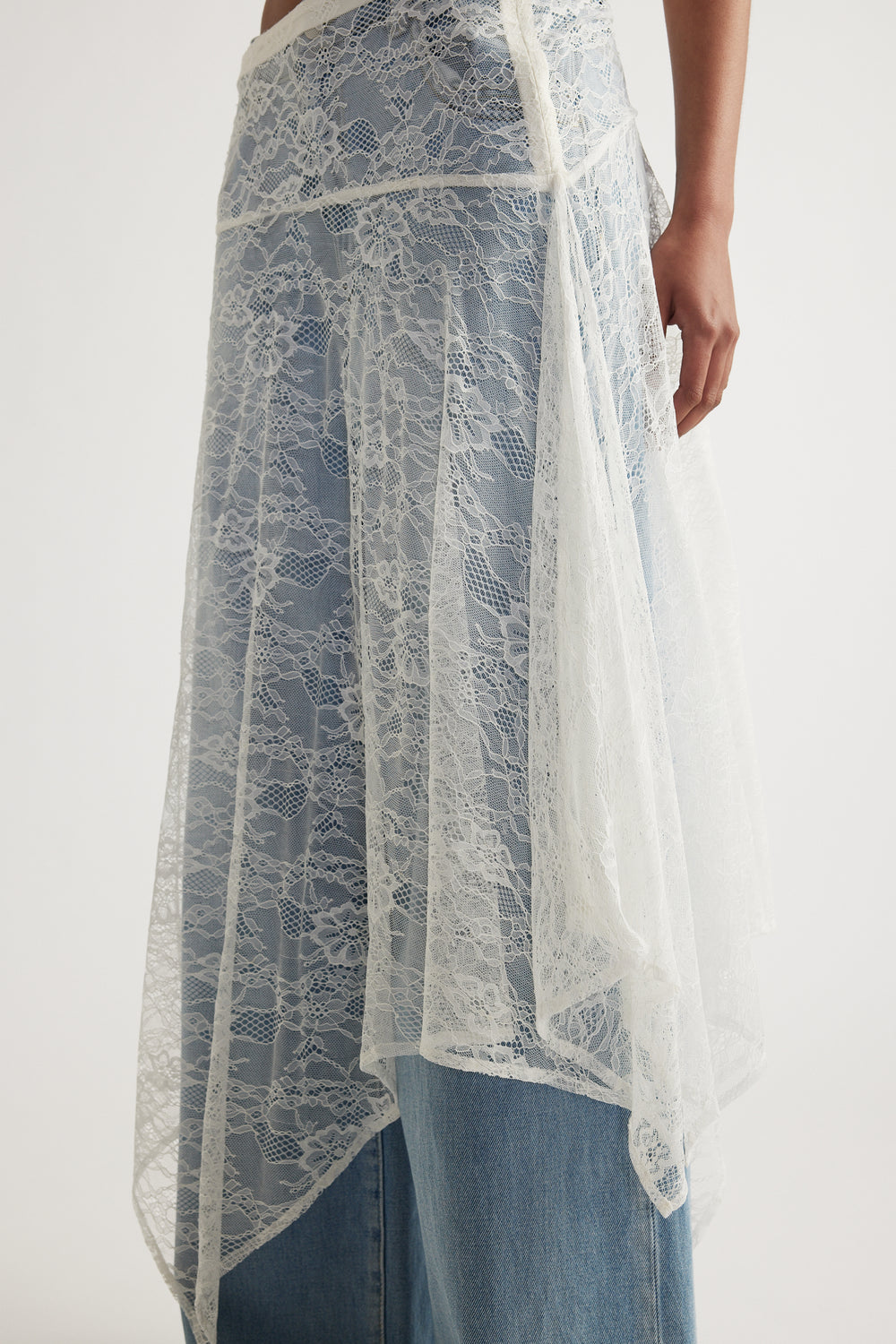 Woman wearing a white lace skirt with an asymmetric hem layered over blue jeans
