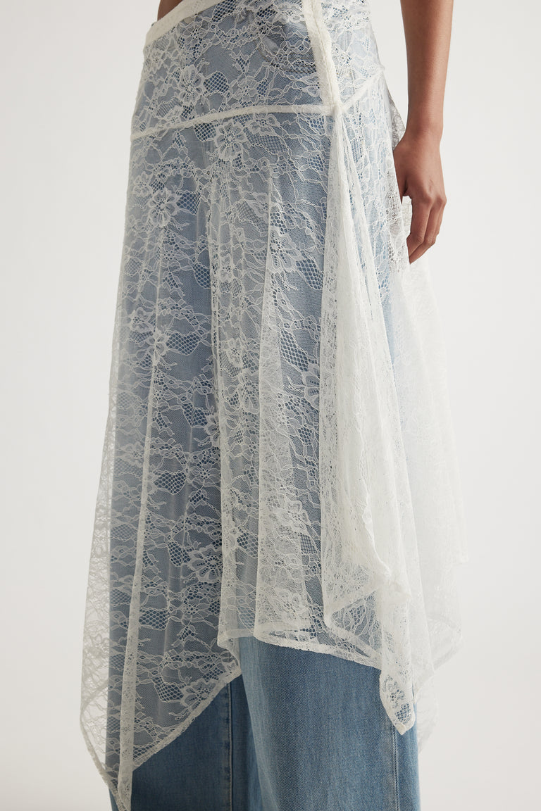 Woman wearing a white lace skirt with an asymmetric hem layered over blue jeans