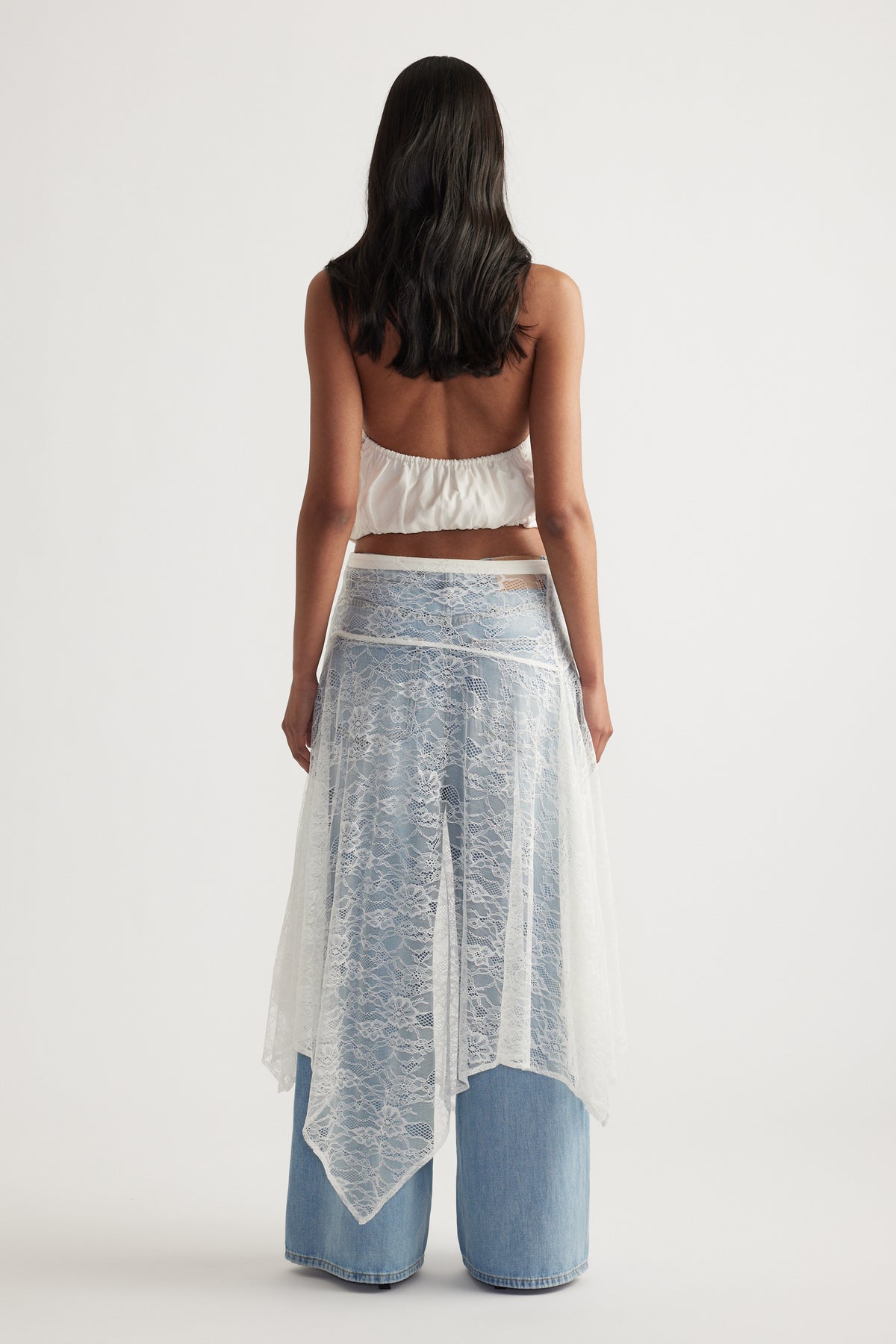 Woman viewed from behind wearing a white lace midi skirt over wide leg blue jeans and a cropped white top