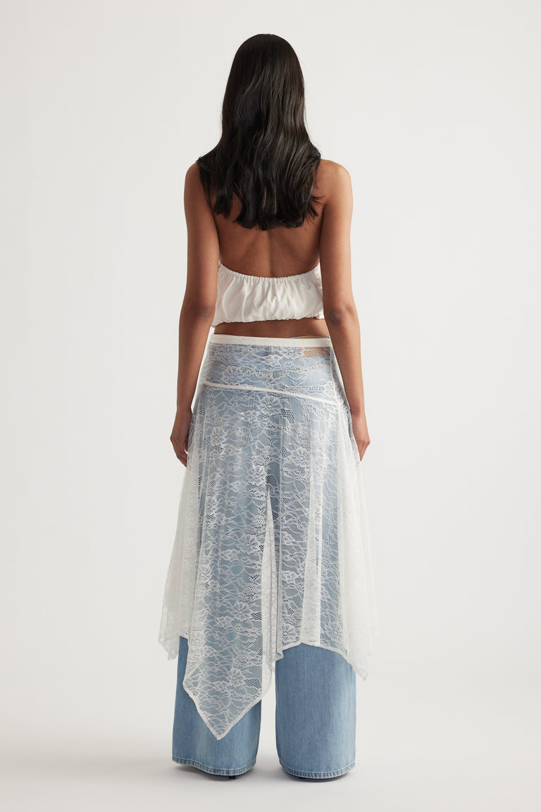 Woman viewed from behind wearing a white lace midi skirt over wide leg blue jeans and a cropped white top