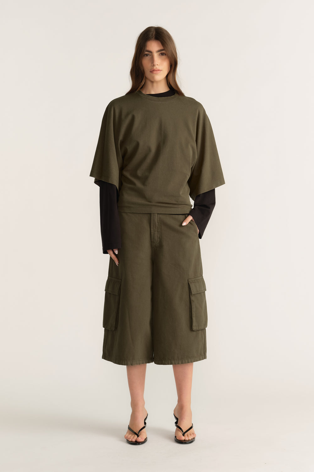 Woman wearing an olive D Luxe relaxed tee with batwing sleeves over a black long sleeve top and cargo shorts