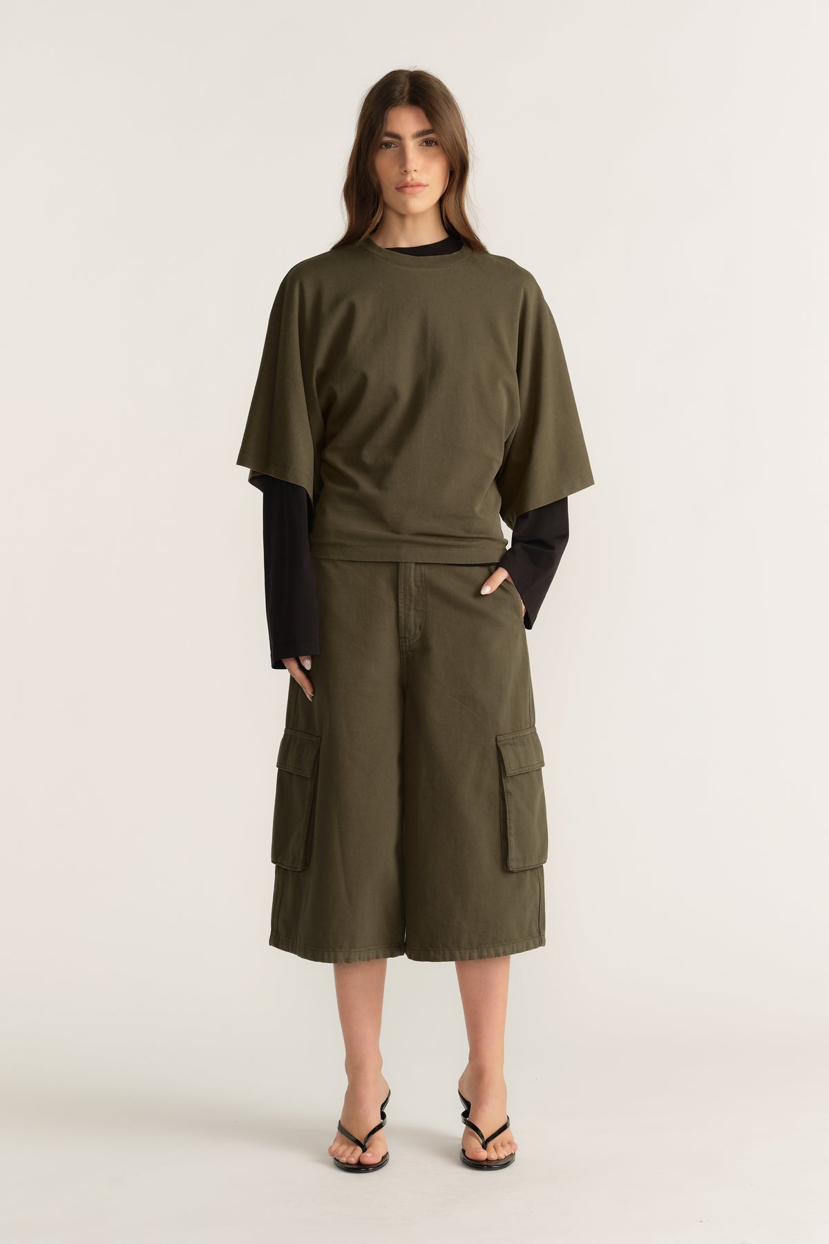 Woman wearing an olive D Luxe relaxed tee with batwing sleeves over a black long sleeve top and cargo shorts