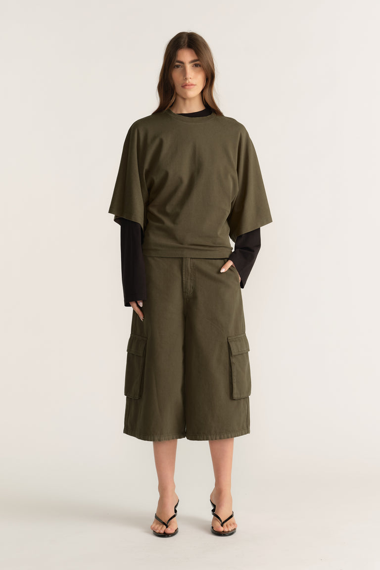 Woman wearing an olive D Luxe relaxed tee with batwing sleeves over a black long sleeve top and cargo shorts