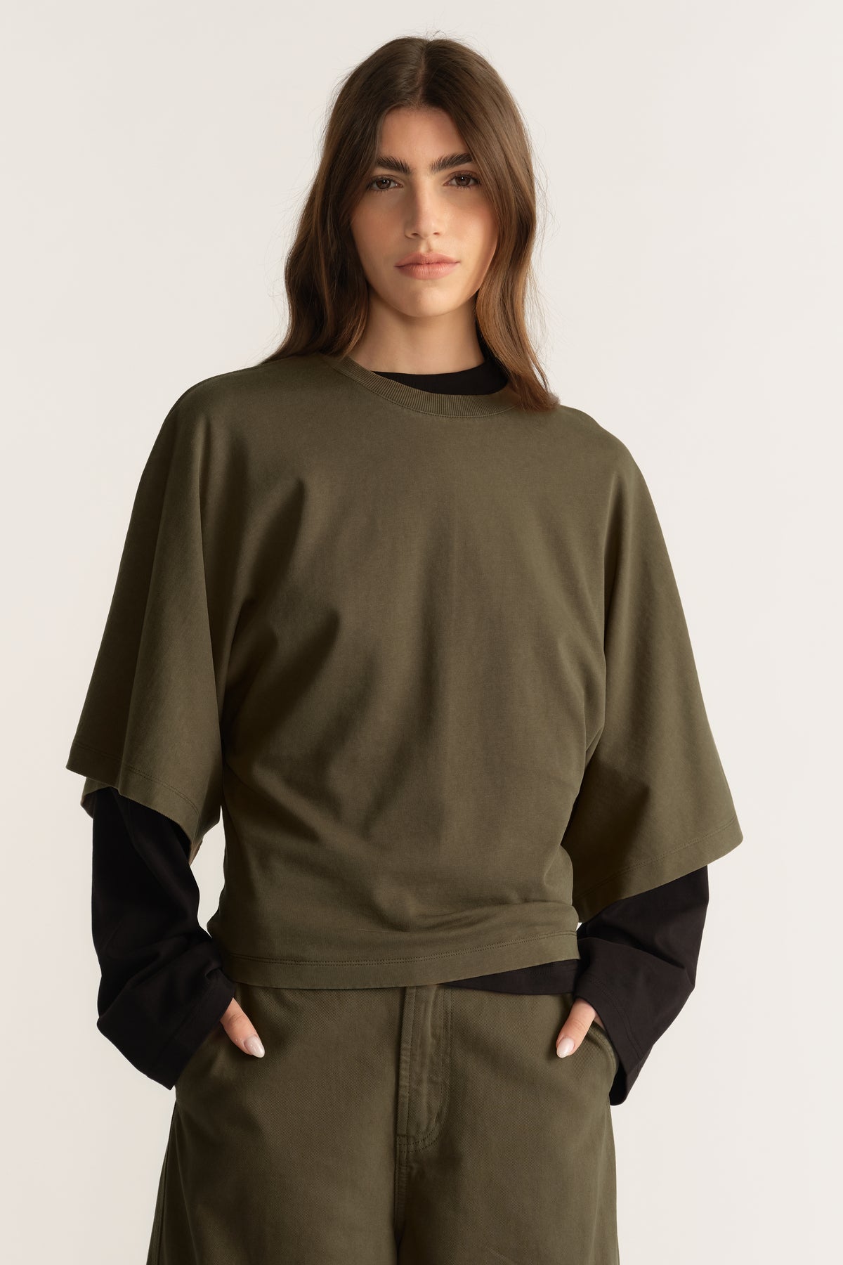 Woman wearing an olive relaxed fit tee with batwing sleeves layered over a black long sleeve top and matching pants