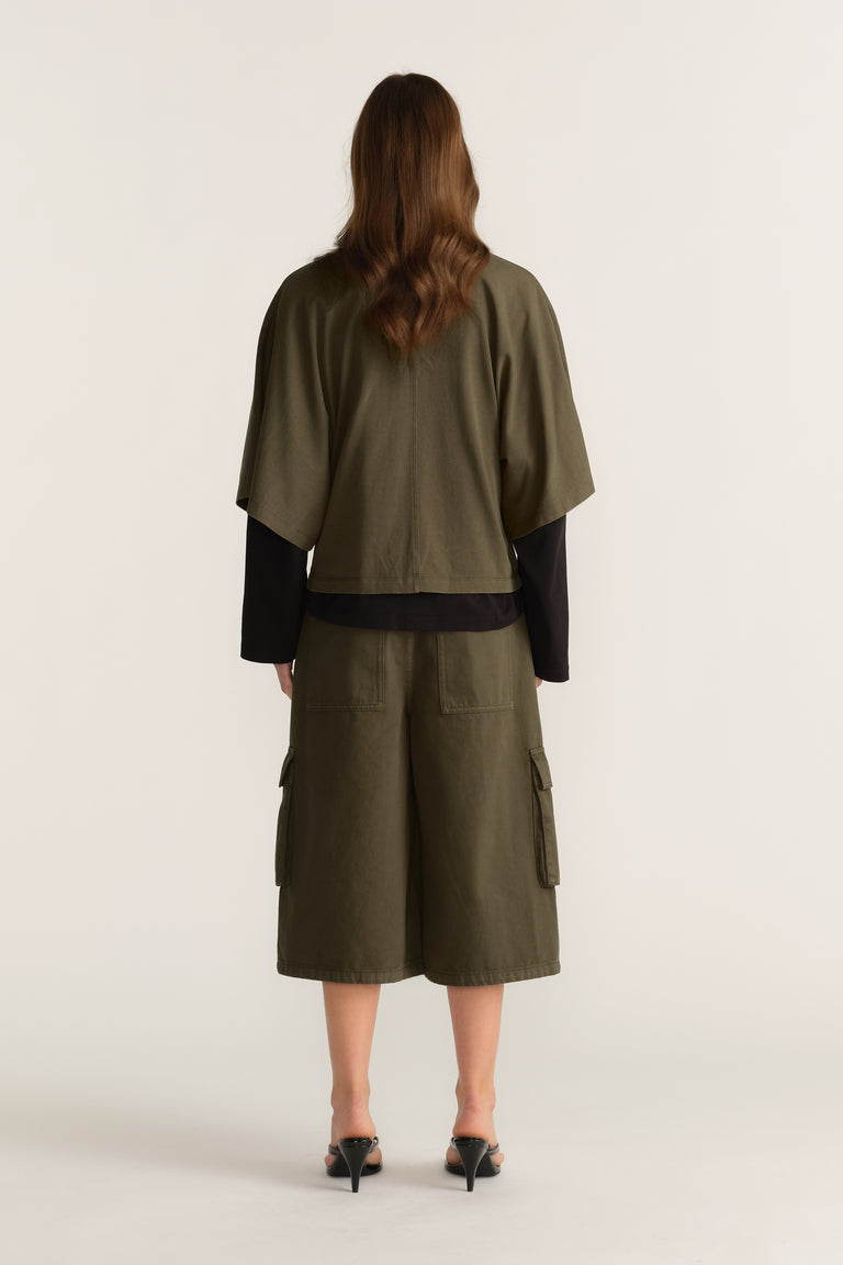 Woman viewed from behind wearing an olive relaxed tee over a black long sleeve top, matching cargo shorts and heels