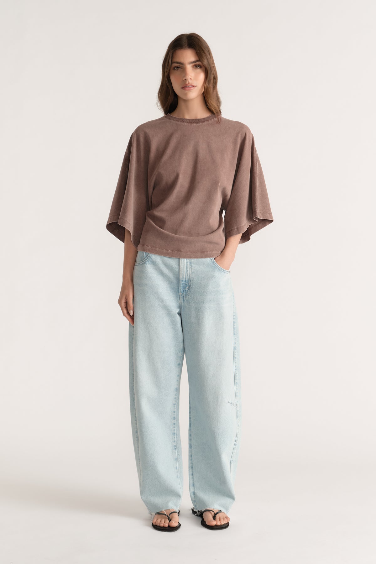 Woman wearing a brown relaxed fit tee with batwing sleeves, light wash wide leg jeans and black sandals