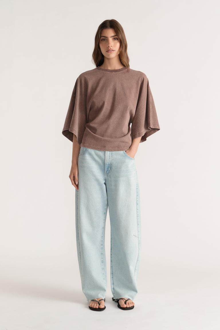 Woman wearing a brown relaxed fit tee with batwing sleeves, light wash wide leg jeans and black sandals