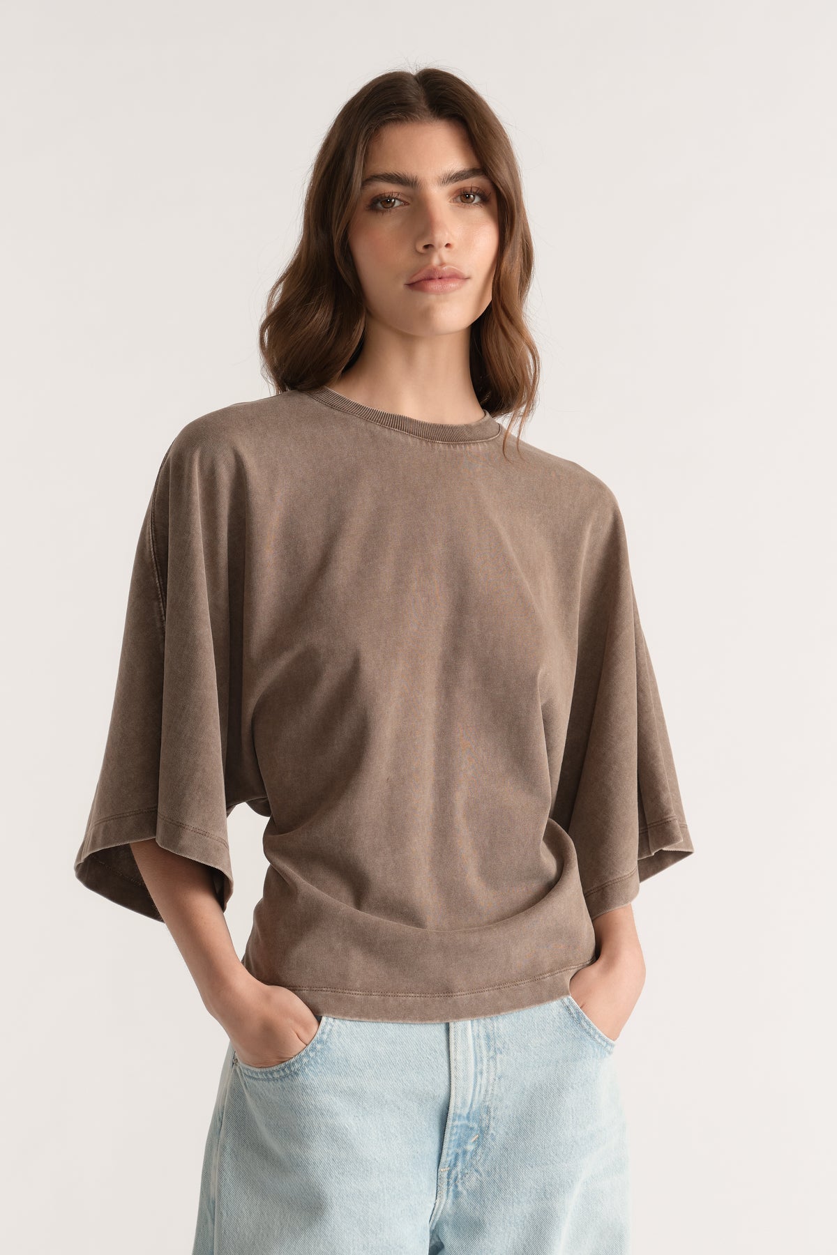 Woman wearing a brown relaxed fit tee with batwing sleeves and light wash jeans