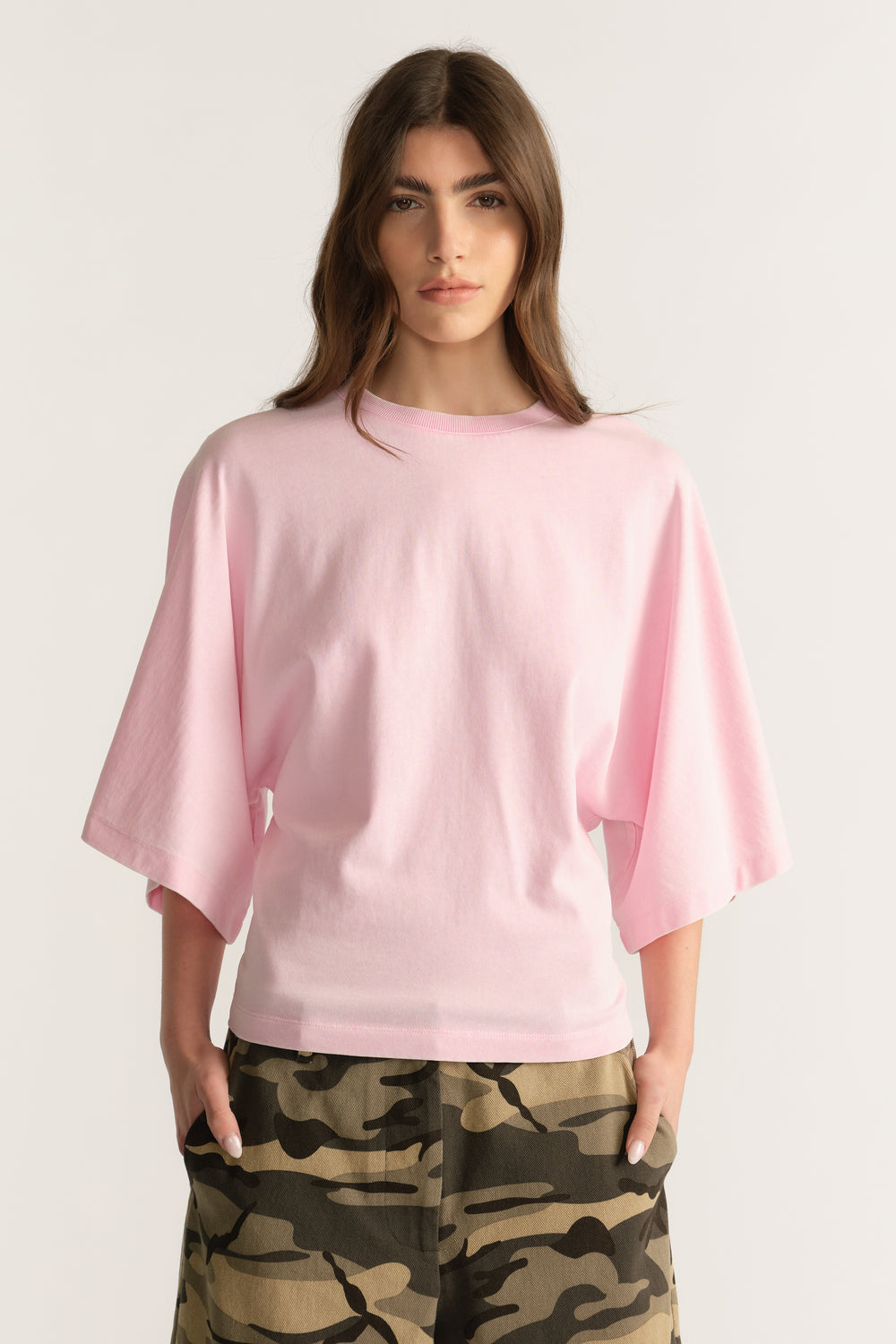 Woman wearing a pale pink relaxed tee with batwing sleeves and camouflage pants