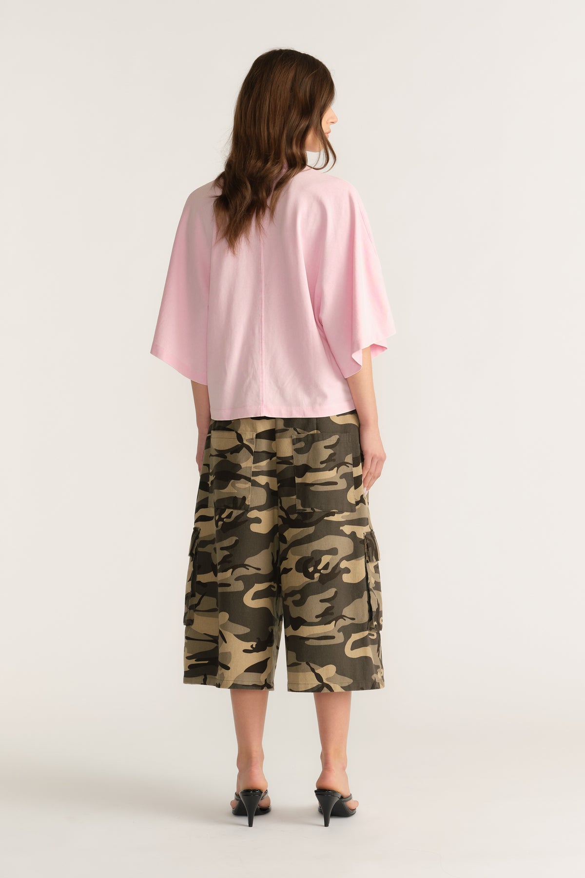 Woman wearing a pink relaxed fit tee with batwing sleeves and camouflage knee length shorts