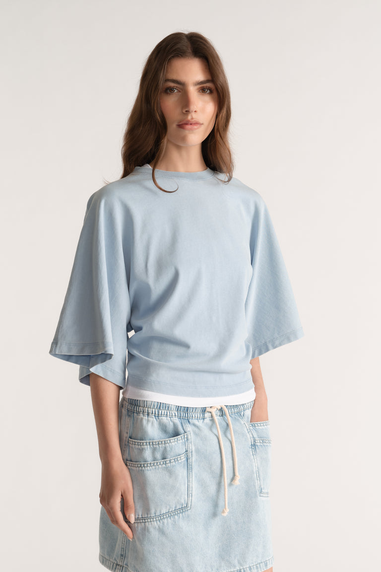 Woman wearing a pale blue relaxed fit tee with batwing sleeves and light wash denim shorts