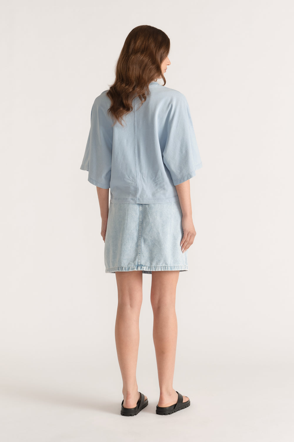 Woman wearing a light blue relaxed fit tee with drop shoulders and a denim skirt, viewed from behind