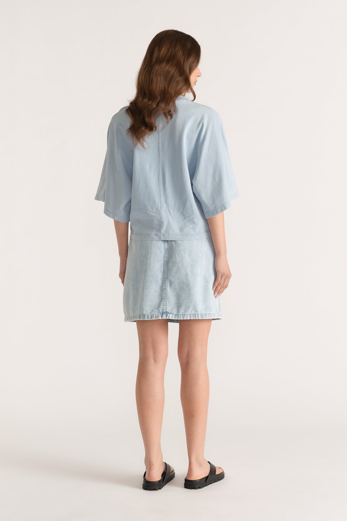 Woman wearing a light blue relaxed fit tee with drop shoulders and a denim skirt, viewed from behind