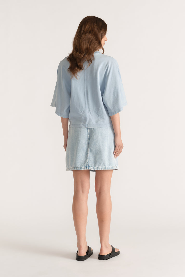 Woman wearing a light blue relaxed fit tee with drop shoulders and a denim skirt, viewed from behind