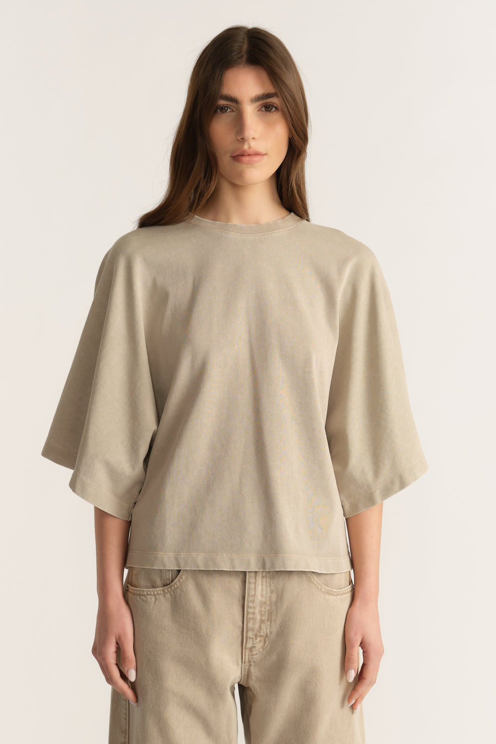 Woman wearing a beige relaxed fit tee with batwing sleeves and matching denim jeans