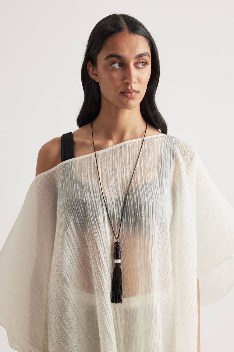 Woman wearing a sheer white pleated top with a long beaded black tassel pendant necklace