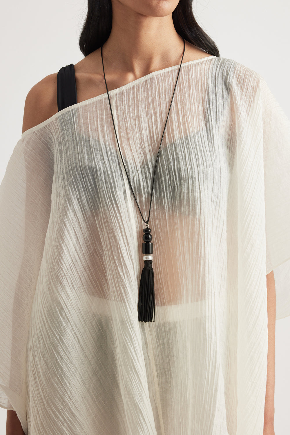 Woman wearing a long beaded black tassel pendant necklace over a sheer white top