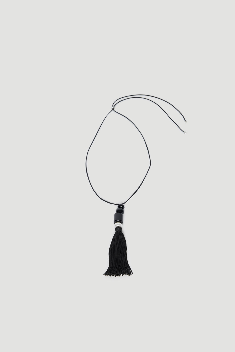Black cord necklace with beaded pendant and tassel drop on a light background