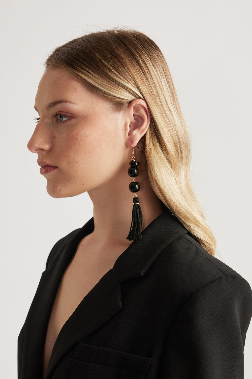 Woman wearing statement black beaded tassel drop earrings with a black blazer