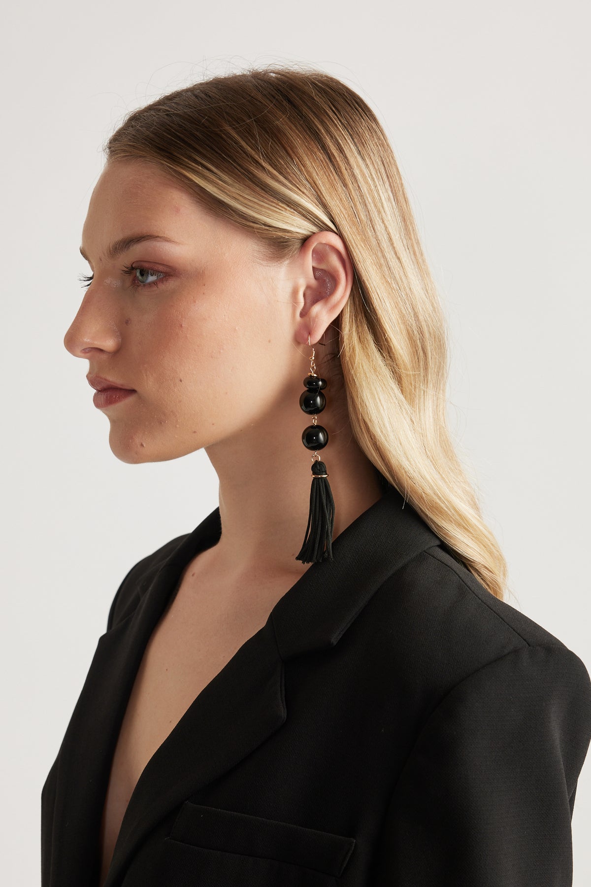Woman wearing statement black beaded tassel drop earrings with a black blazer