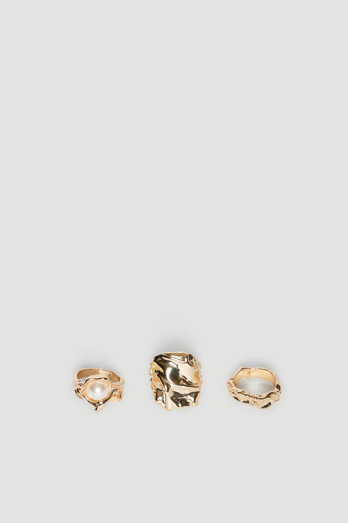 Three gold stackable rings with irregular shapes, including one with a pearl accent