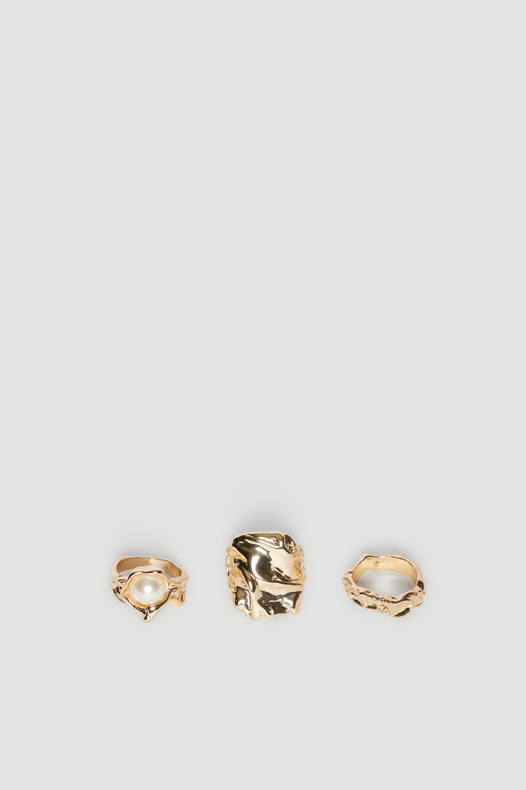 Three gold stackable rings with irregular shapes, including one with a pearl accent