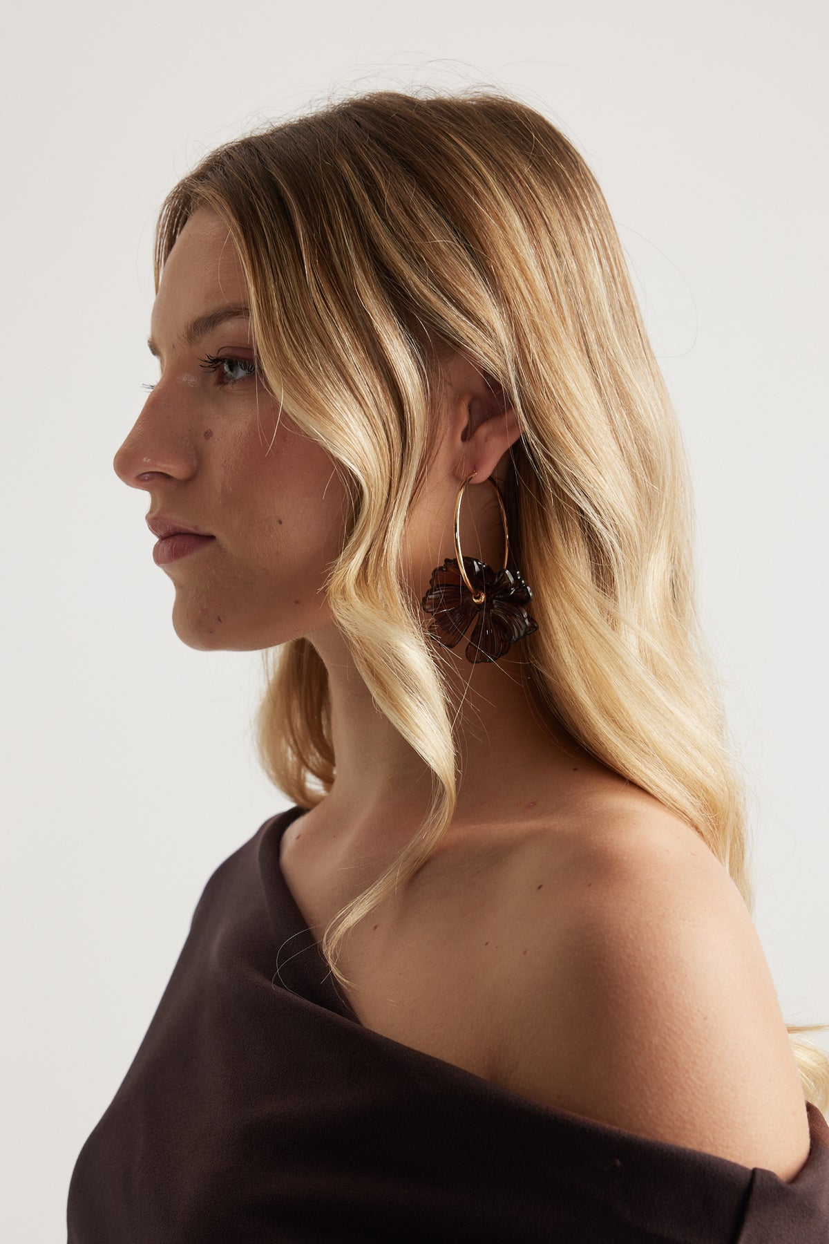 Woman wearing a statement gold flower hoop earring with a layered floral pendant