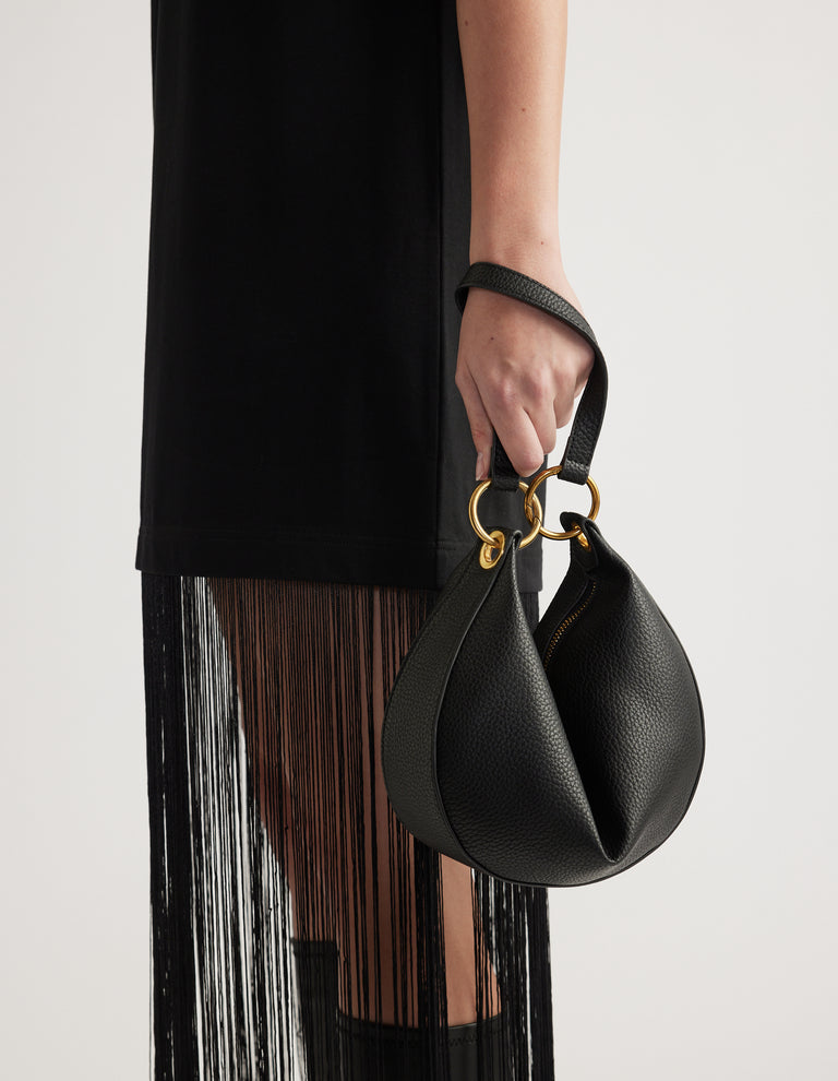 Black half moon bag with gold hardware held by a woman wearing a black fringed skirt