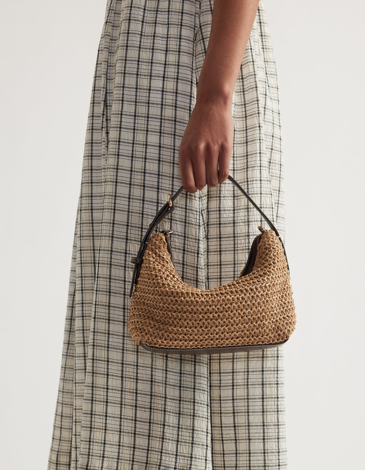 Brown paper weave crossbody bag with a dark strap, held against a checked dress