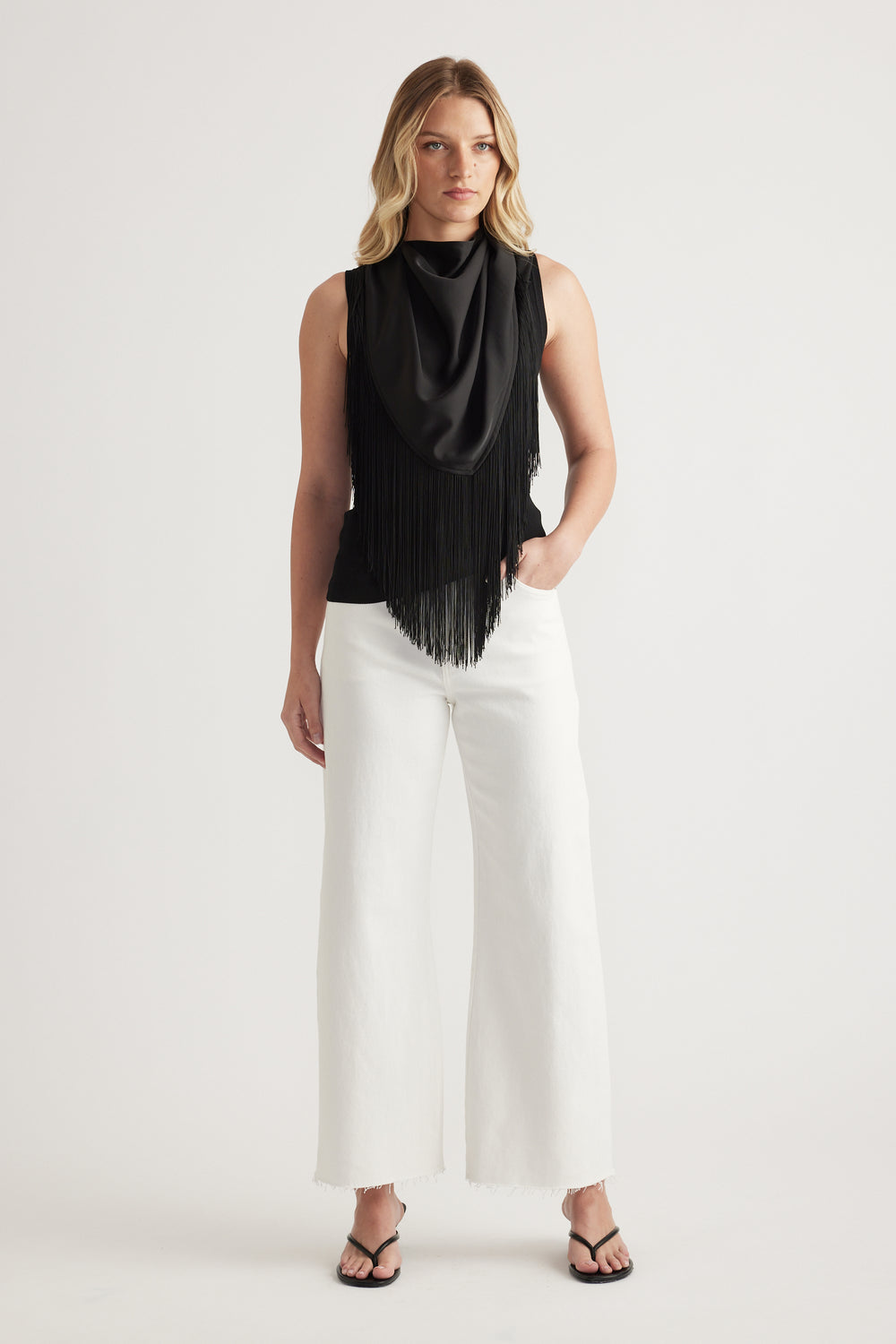 Woman wearing white high rise wide leg jeans with raw hems, a black sleeveless top and sandals