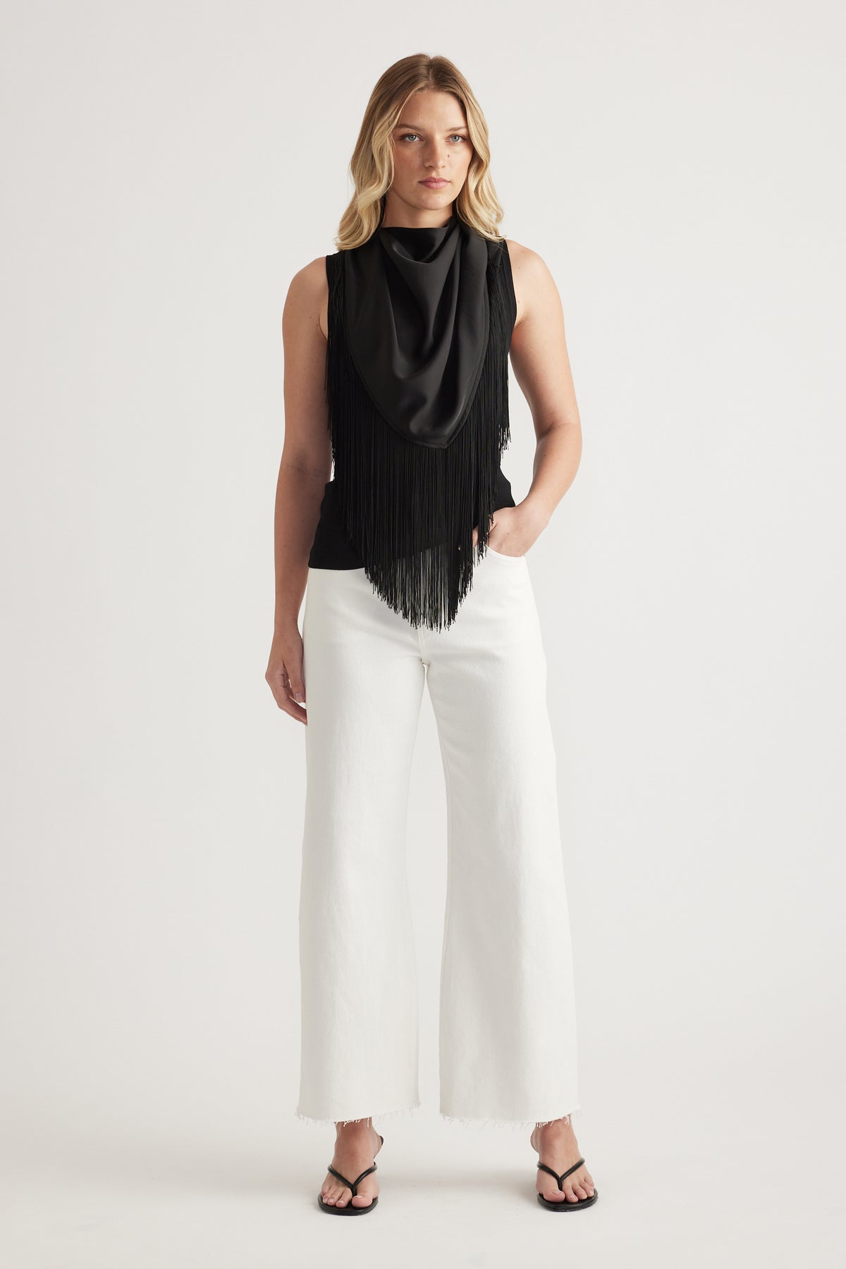 Woman wearing white high rise wide leg jeans with raw hems, a black sleeveless top and sandals