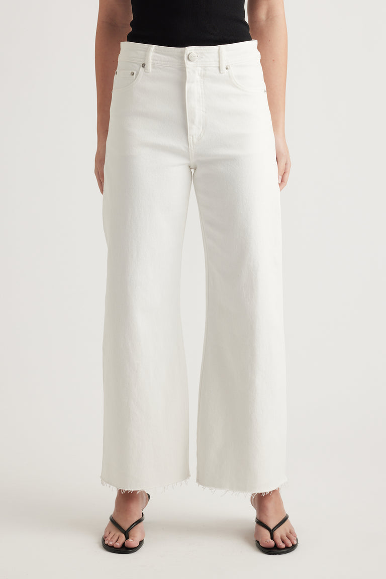 Woman wearing high rise white wide leg jeans with raw hems, a black top and black sandals