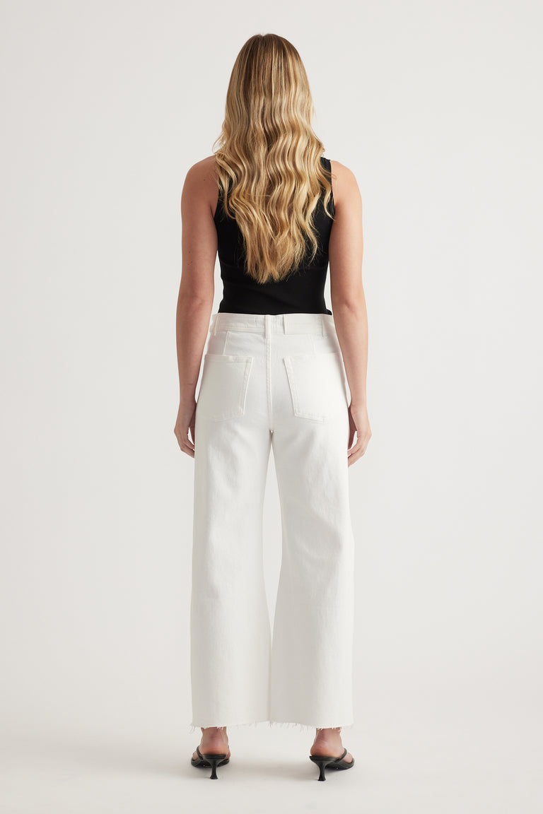 Woman viewed from behind wearing white wide leg jeans with raw hems, a black sleeveless top and heels