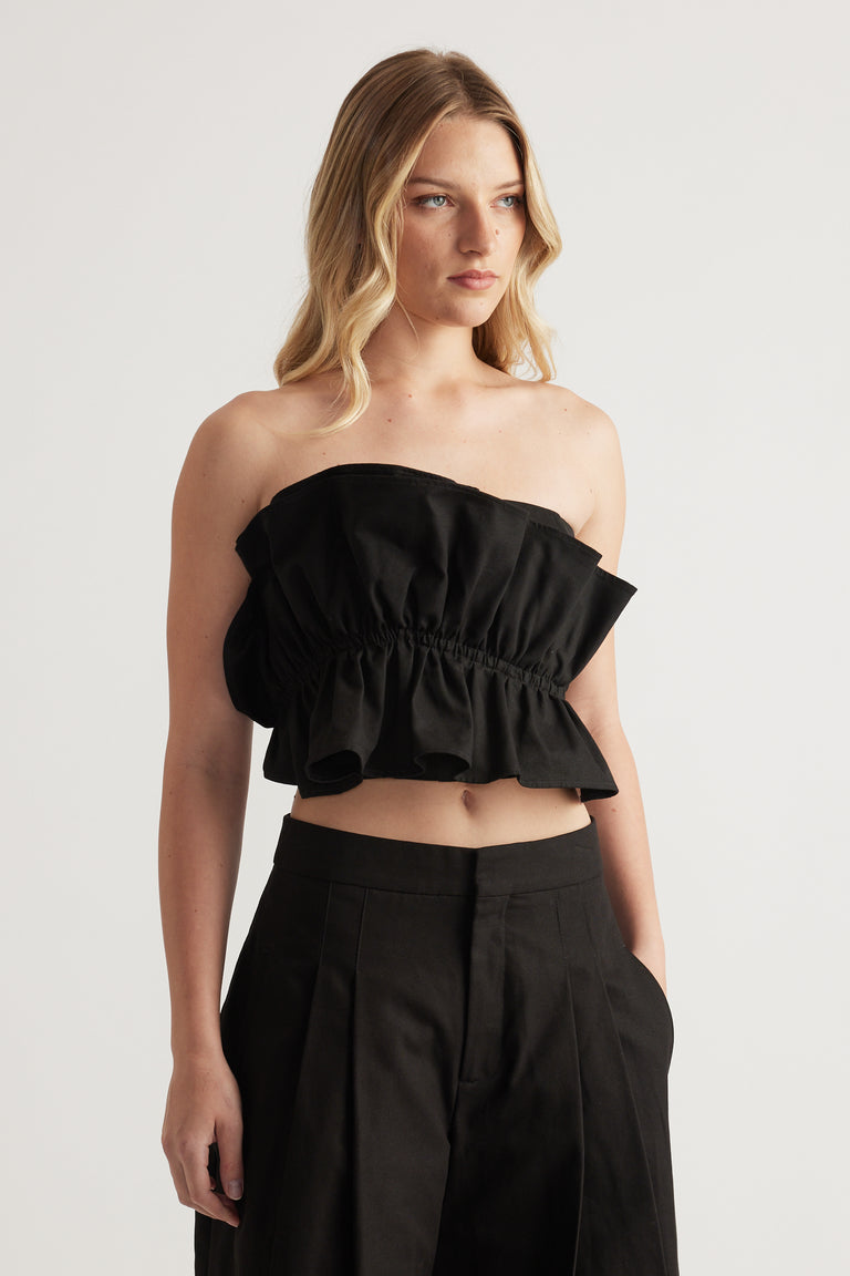 Woman wearing a black strapless ruffle top with high waisted pleat pants