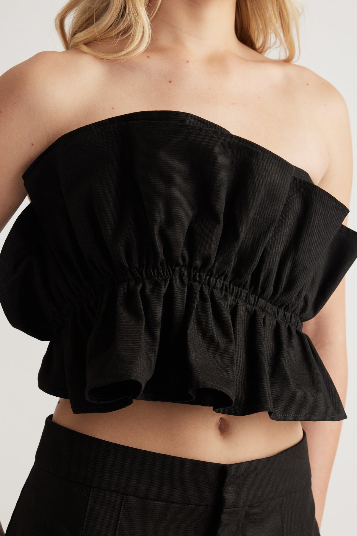 Woman wearing a black strapless cropped top with ruffle detailing and matching black pants