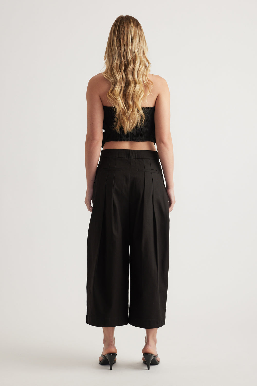 Back view of a woman wearing a black strapless cropped top with wide leg pants and black heels