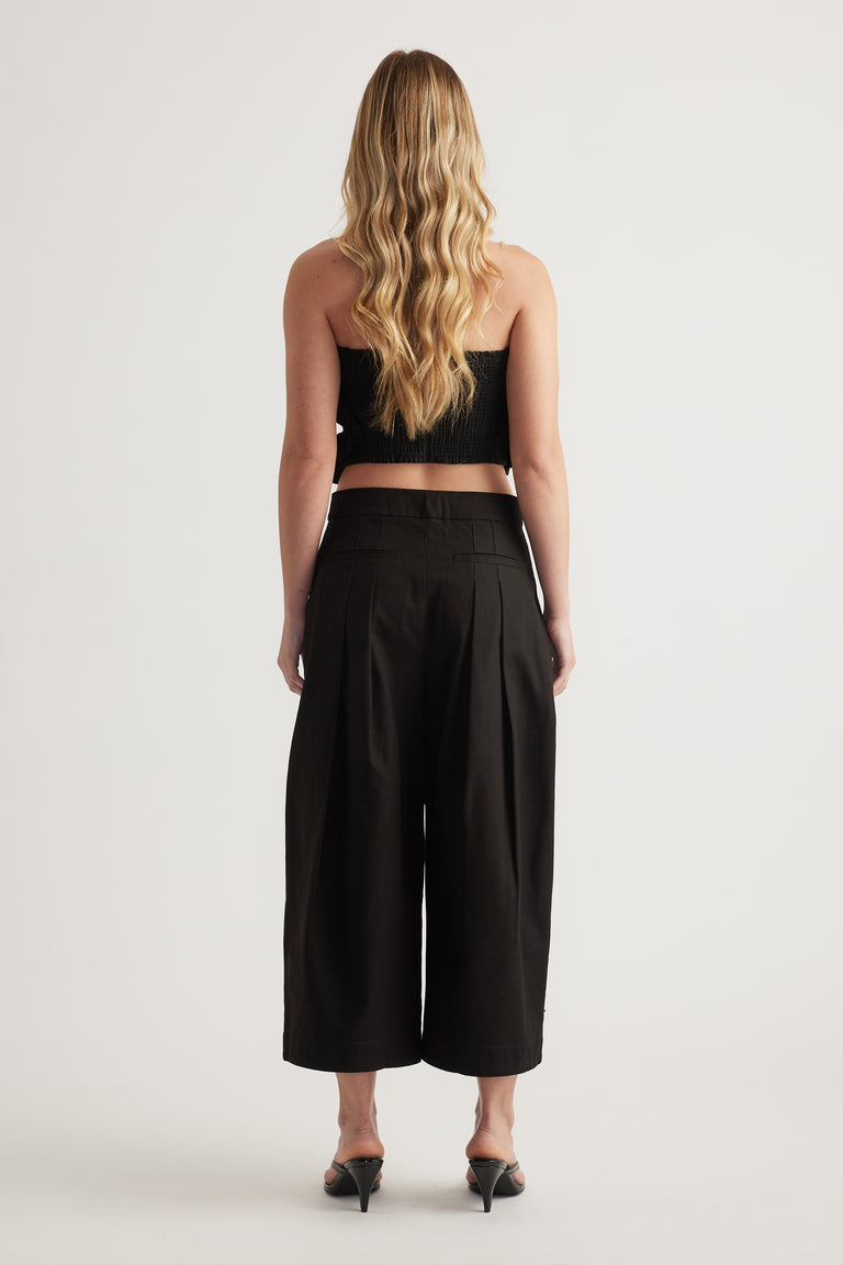 Back view of a woman wearing a black strapless cropped top with wide leg pants and black heels