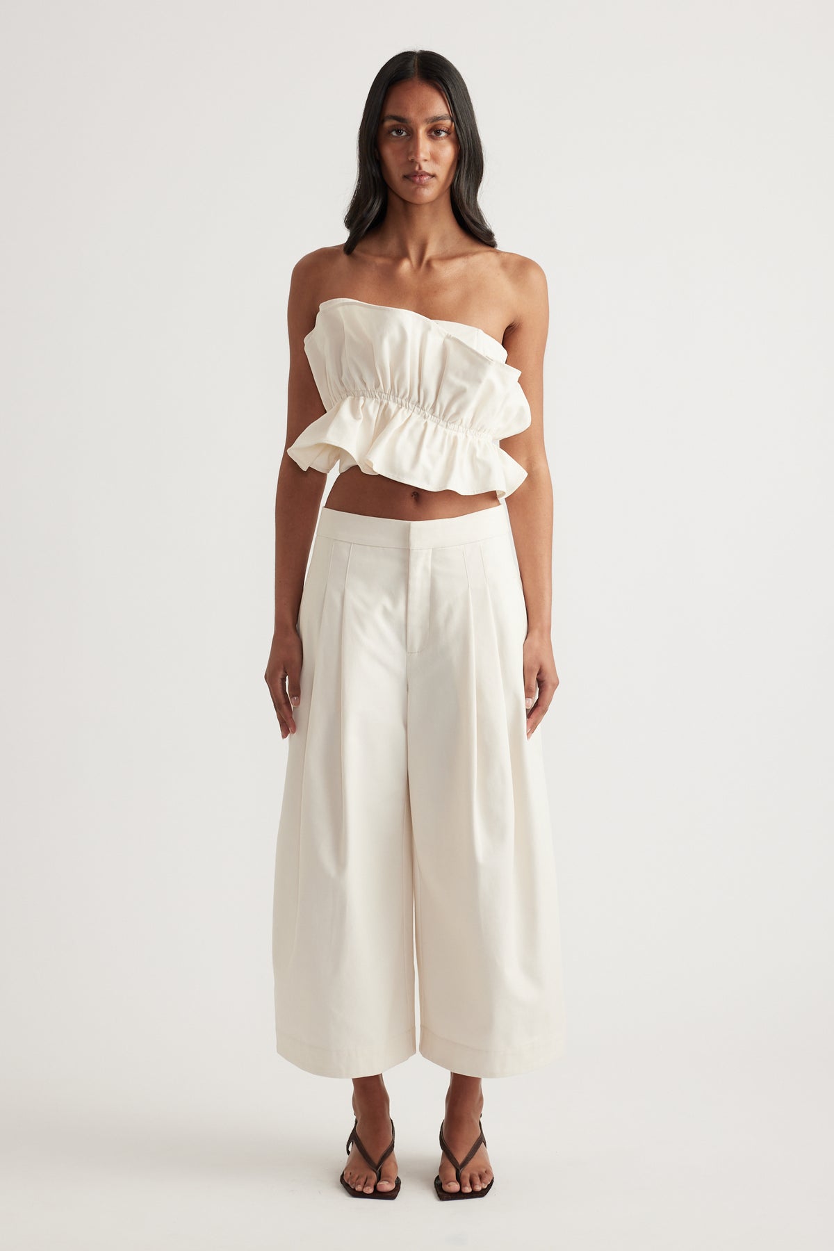Woman in a white strapless ruffle top with wide leg pants and black strappy sandals