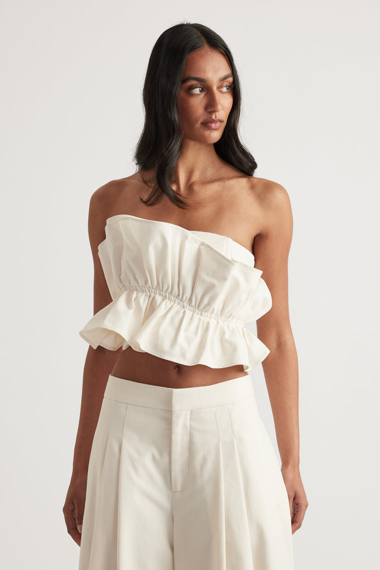Woman wearing a cream strapless ruffle top with white pleated pants