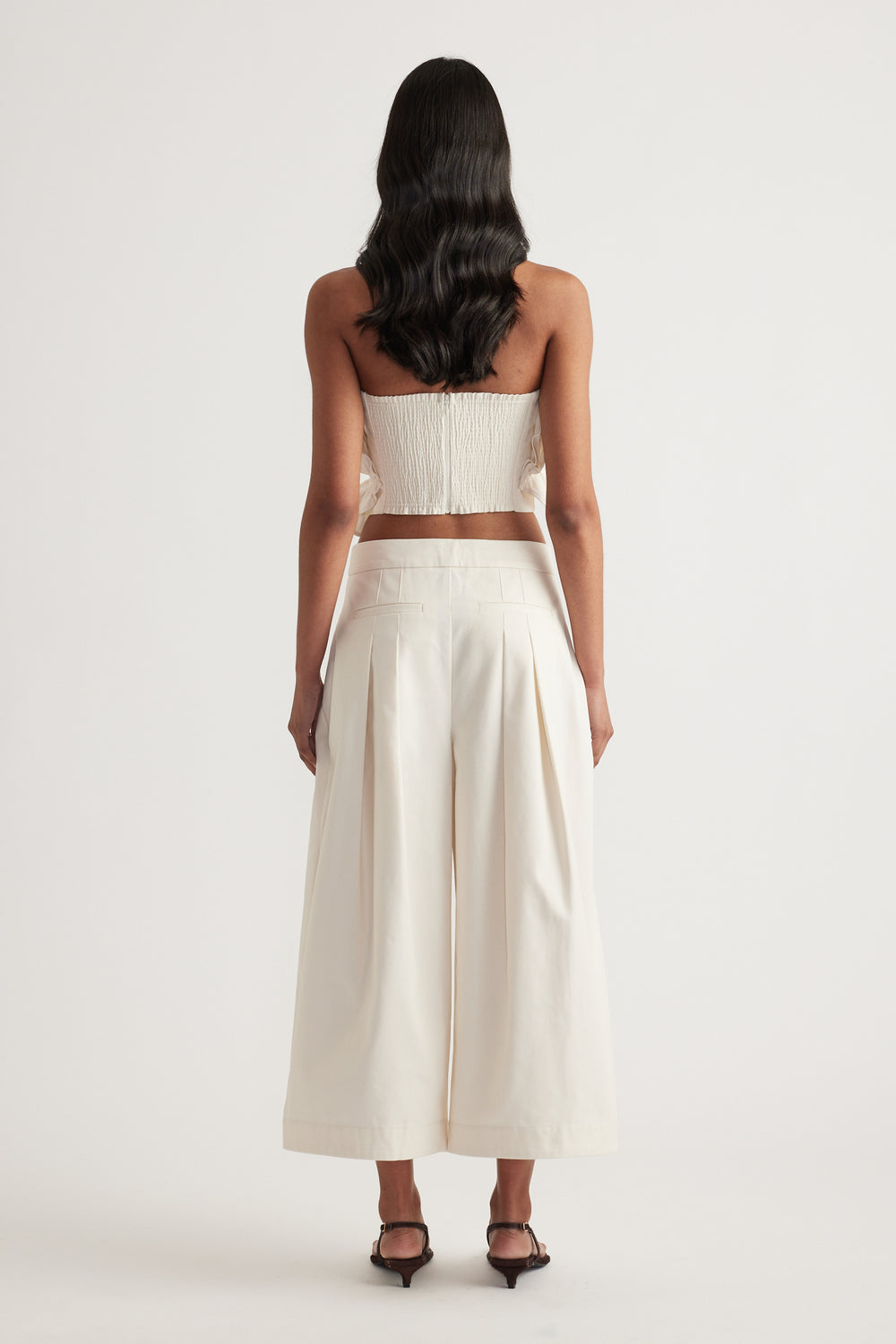 Back view of a woman wearing an ivory strapless cropped top with wide leg pleat pants and black heels