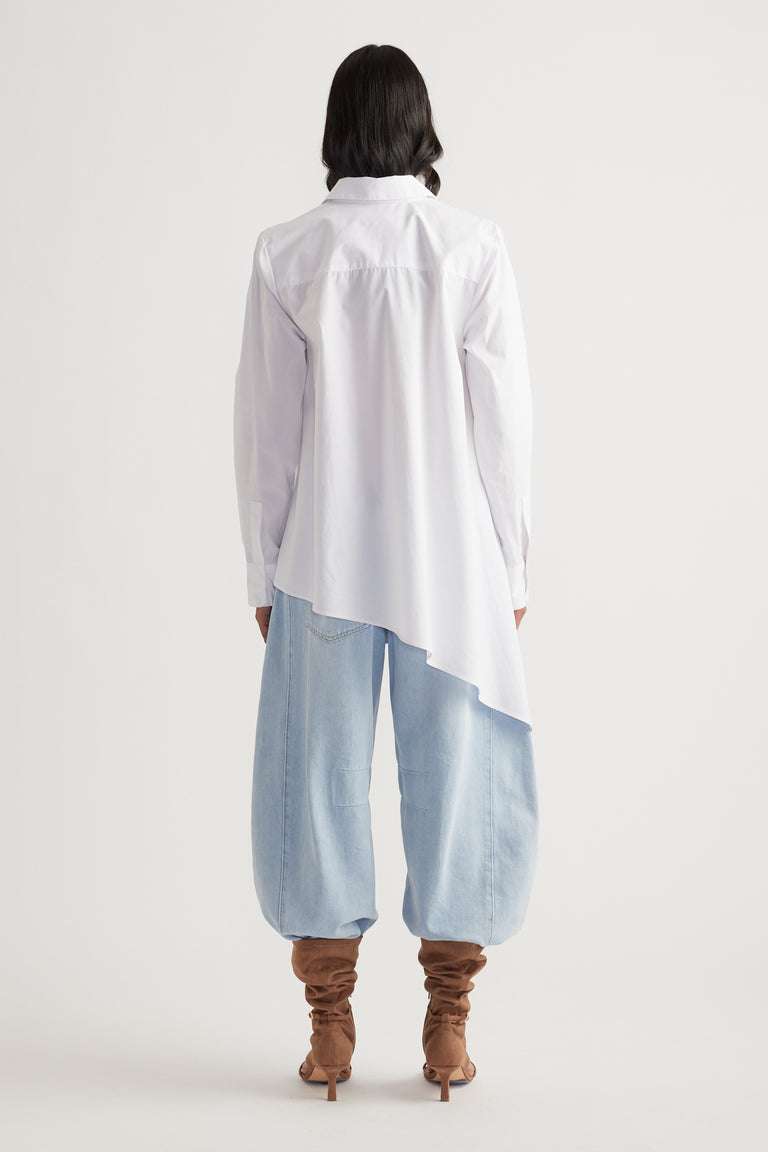 Woman seen from behind wearing a white asymmetric shirt paired with loose light-wash denim pants and slouchy brown boots