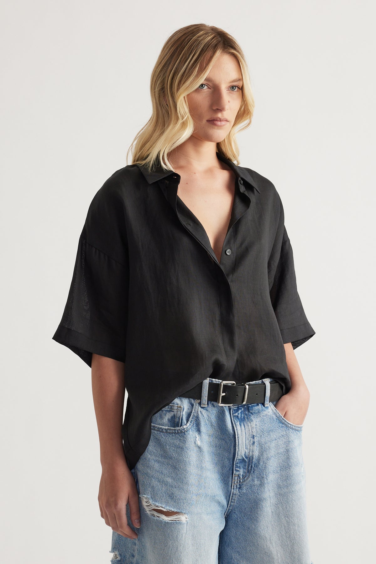 Woman wearing an oversized black collared button up shirt with relaxed sleeves and ripped light blue jeans