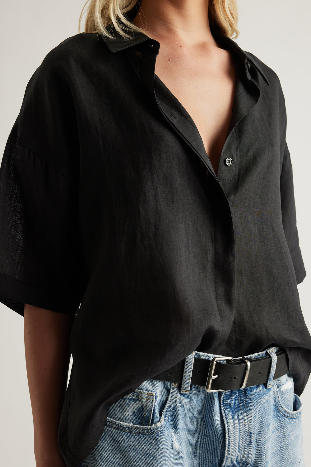 Woman wearing a black oversized collared button up shirt styled with blue jeans