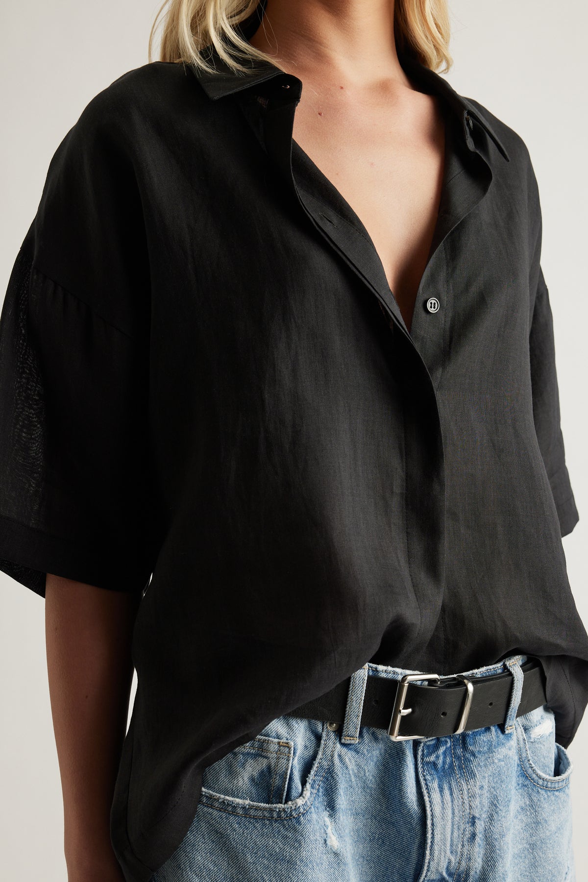 Woman wearing a black oversized collared button up shirt styled with blue jeans