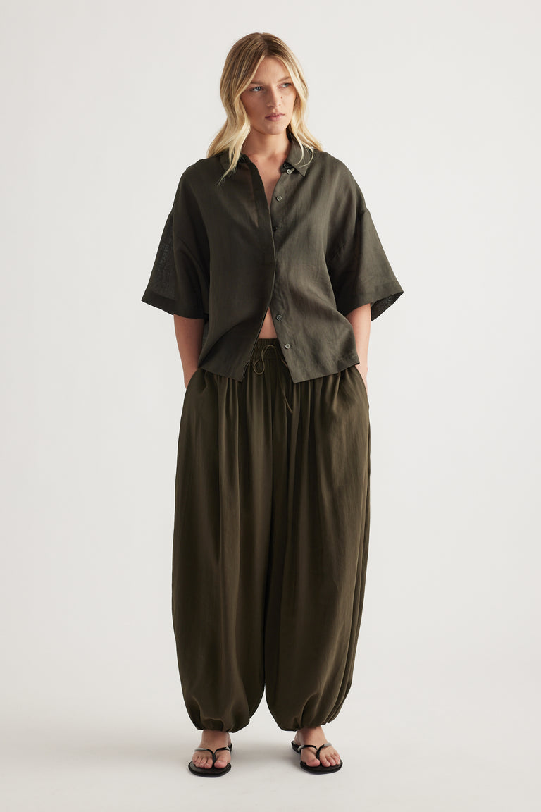 Woman wearing an oversized olive collared shirt with relaxed drawstring pants and strappy sandals