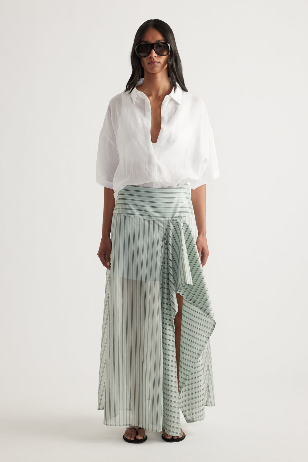 Woman wearing an oversized white collared shirt with a striped wrap maxi skirt and sunglasses