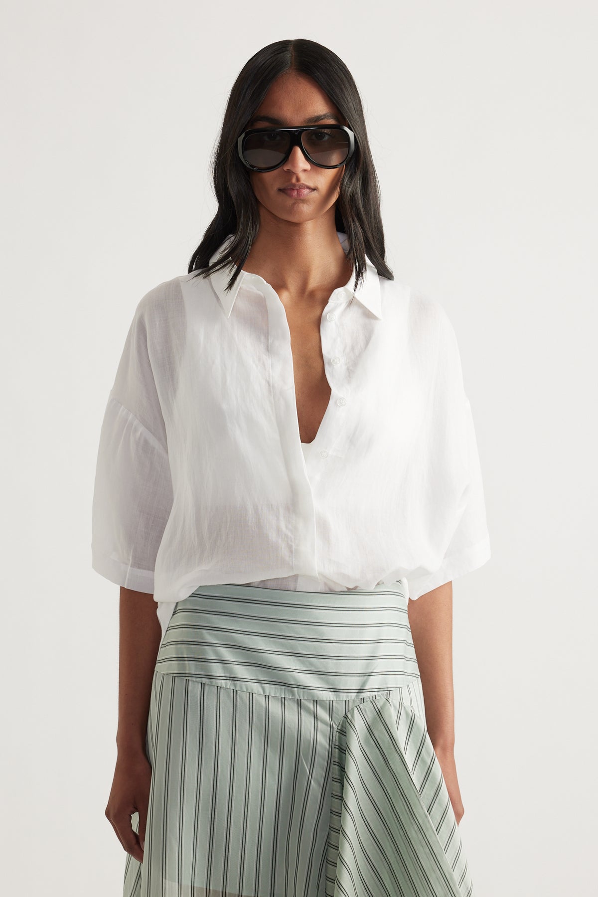 Woman wearing an oversized white collared button up shirt with rolled sleeves, styled with a striped wrap skirt